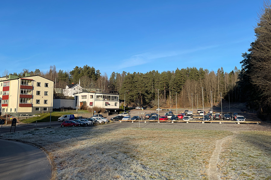 En parkeringsplats full med parkerade bilar. I bakgrunden syns skog och flerfamiljshus.