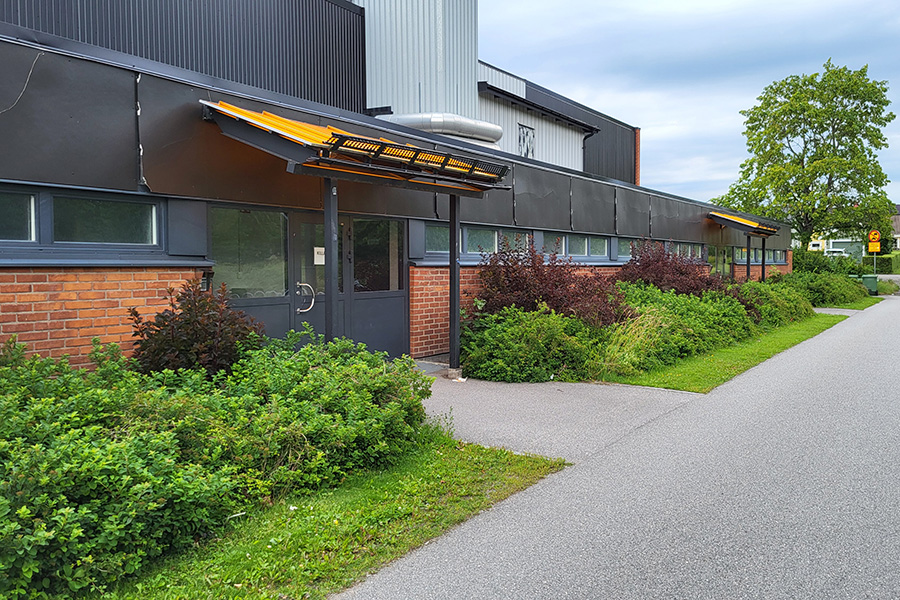 Skolbyggnad i svart och rött tegel med buskar framför och dubbla entrédörrar till idrottshallen.