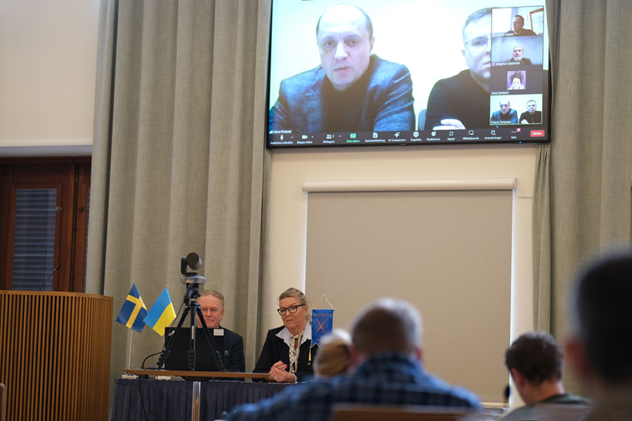 Två personer sitter vid ett bord och två personer är med på videosamtal