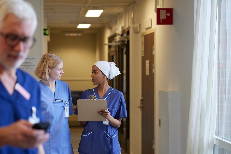 En äldre dam håller i en medicinlåda och en manlig undersköterska ler och lägger armen om henne.