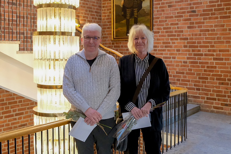 Två personer står i en trappa med varsin ros i handen. 