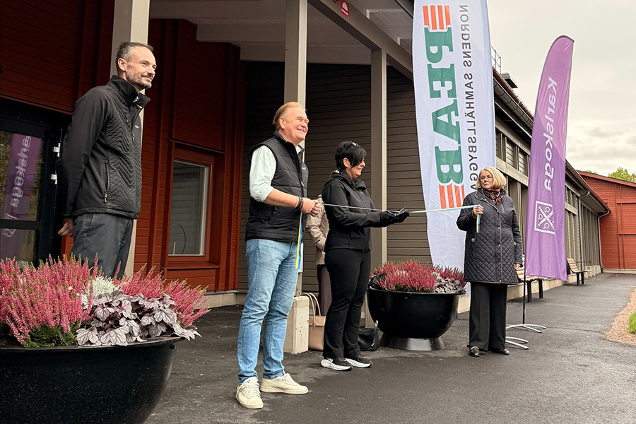 Fyra personer står framför en röd byggnad. Två personer håller upp ett blågult band som en tredje person klipper på mitten med en sax.