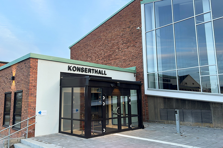 En entré till en fastighet med röd tegelfasad. Över entrén står det Konserthall med versaler. 