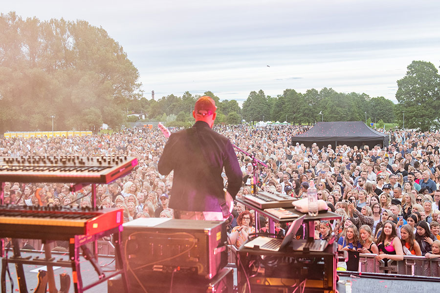 En artist som står på scen och spelar gitarr. I bakgrunden syns ett publikhav.
