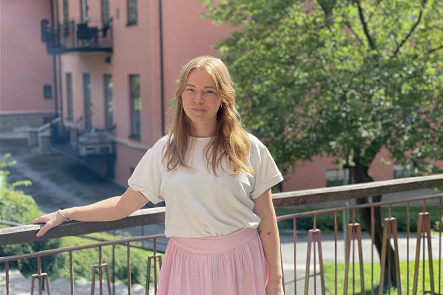 Porträtt tjej som hänger lite ätt på ett staket framför en röd byggnad