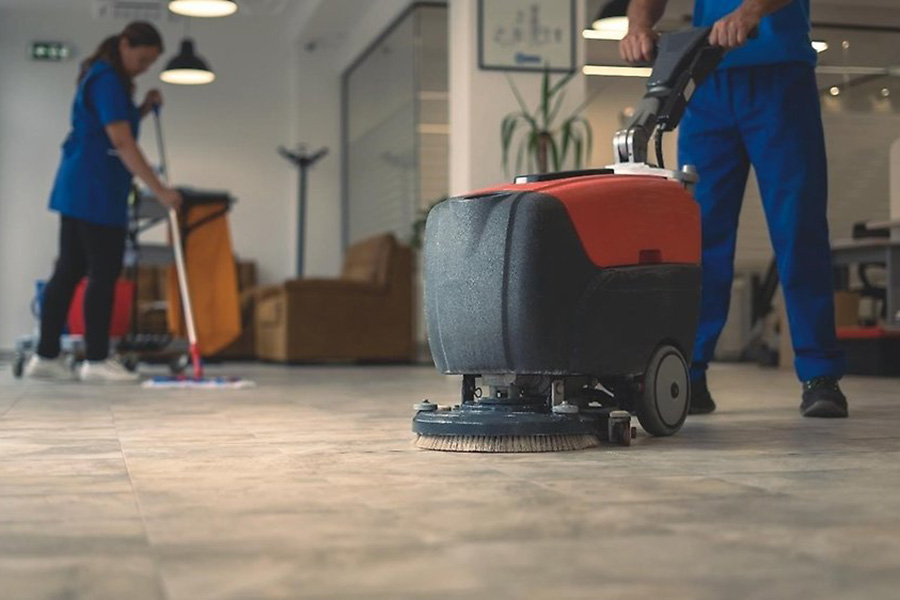 Man kör städmaskin och kvinna moppar golv i bakgrunden.
