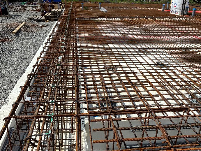 Armeringsjärn arrangerade på en betonggrund, redo för gjutning. Järn och grus syns på sidorna.