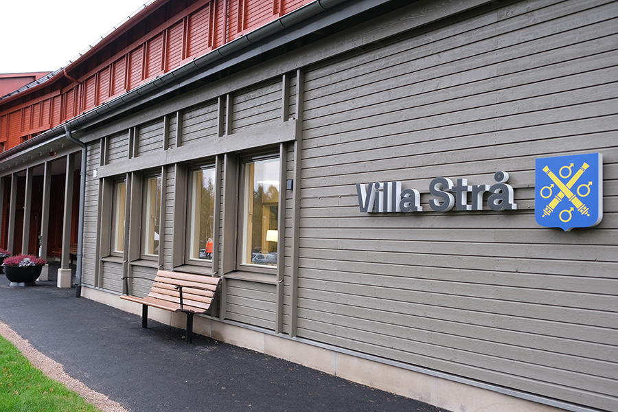 En byggnad med röd och grå träfasad. På väggen finns en skylt där det står "Villa strå"