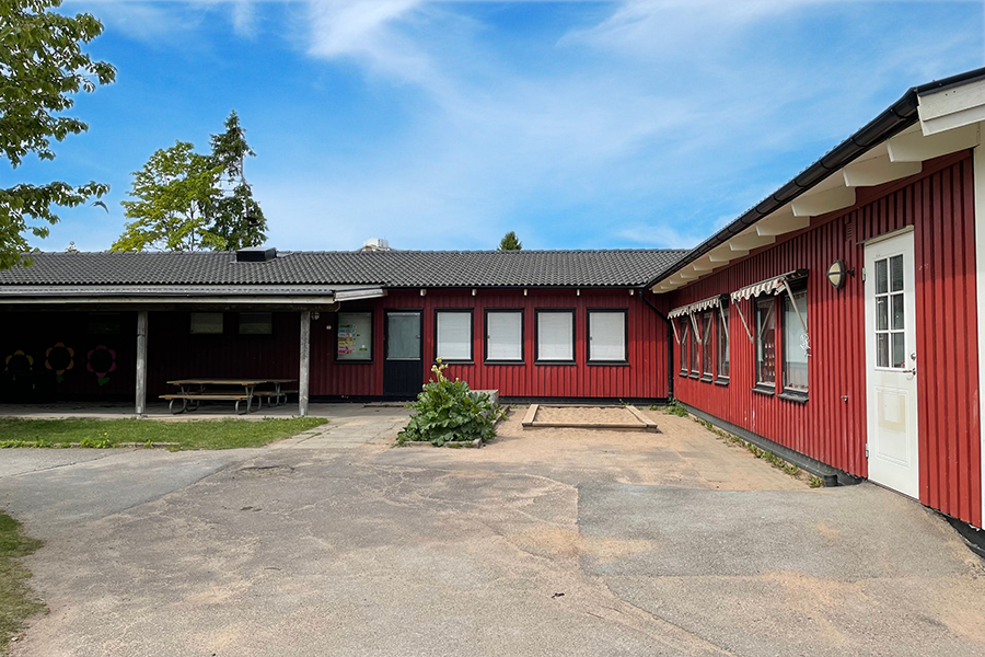 Gullvivans förskola. Röd enplansbyggnad med svart tak och en innergård med asfalt. 