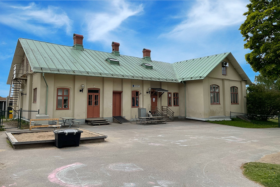 Loviselunds förskola. Bremevit tvåvåningsbyggnad med grönt plåttak. Utanför finns en innegård med asfalt där barn målat med kritor.