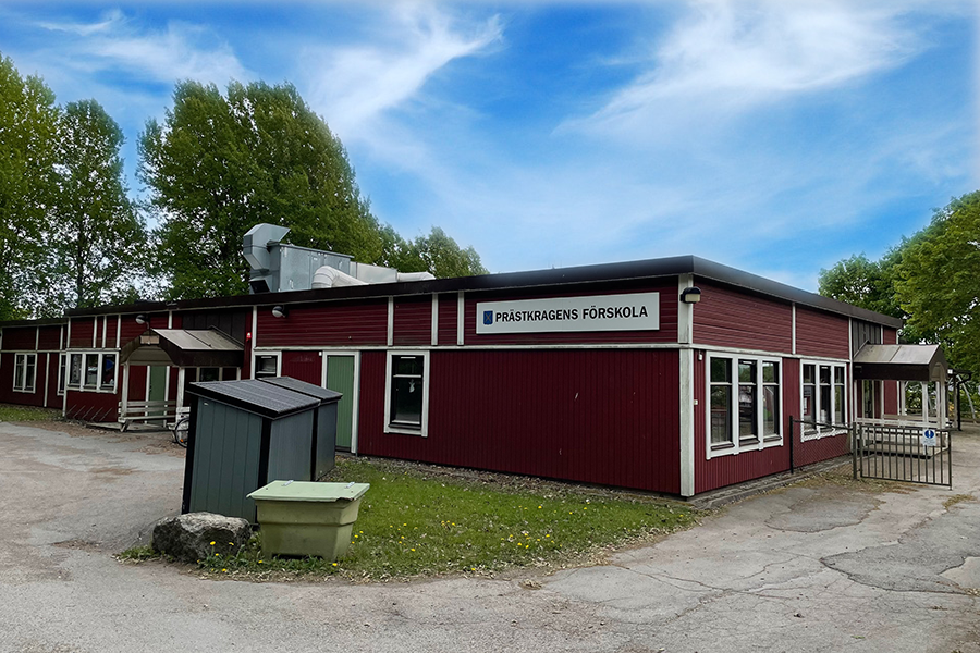 Prästkragens förskola. En röd byggnad med vita knutar och asfalt runt omkring byggnaden. 