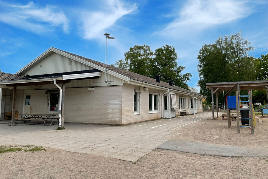 Rävens förskola. En vit tegelbyggnad med randiga markiser och stenplattor runt om byggnaden. 