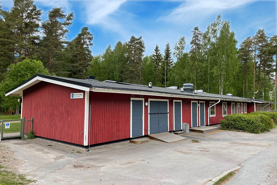 Rödluvans förskola. En röd träbyggnad med vita knutar och blåa dörrar och skogen i bakgrunden. 