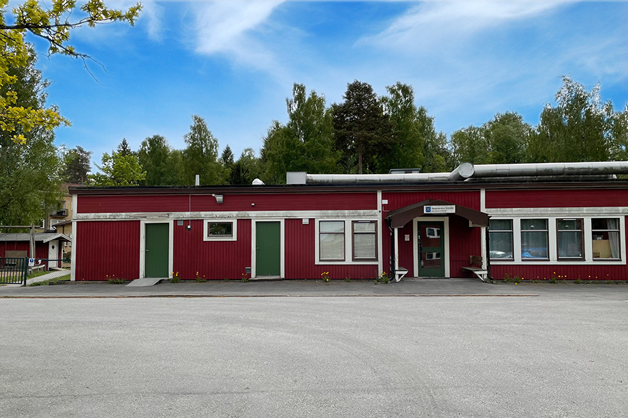 Skogsduvans förskola. En röd byggnad med vita knutar och gröna dörren med asfalt utanför byggnaden. 