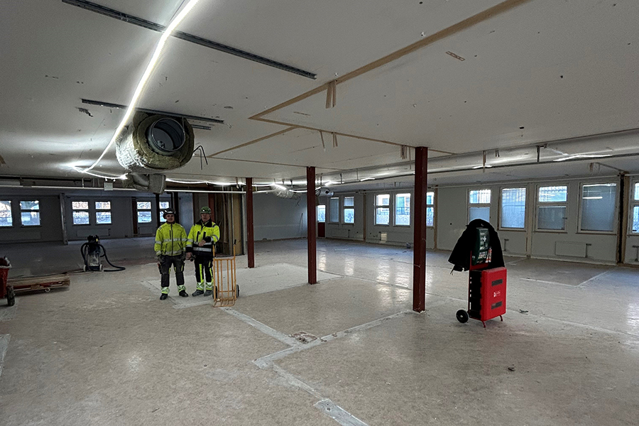 En tom lokal. Till vänster i bild står två personer som är klädda i arbetskläder.
