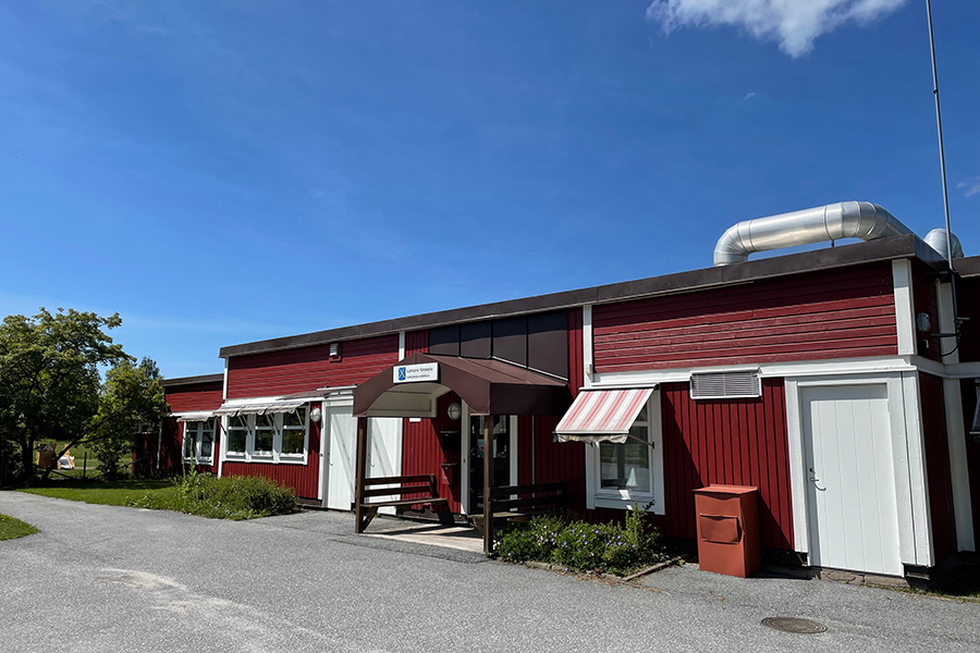 Lärkans förskola. En röd byggnad med asfalt utanför entrén och klarblå himmel. 