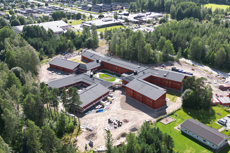 Flygbild över en byggarbetsplats med en byggnad i mitten av bilden. Runtomkring står arbetsmaterial.