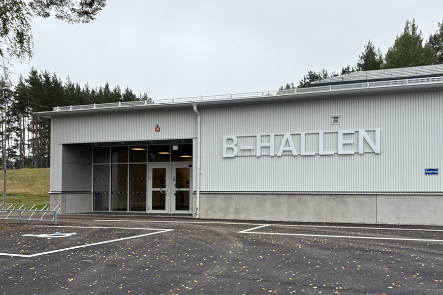 En byggnad med glasdörrar som entré. Till höger om entrén står det B-HALLEN.