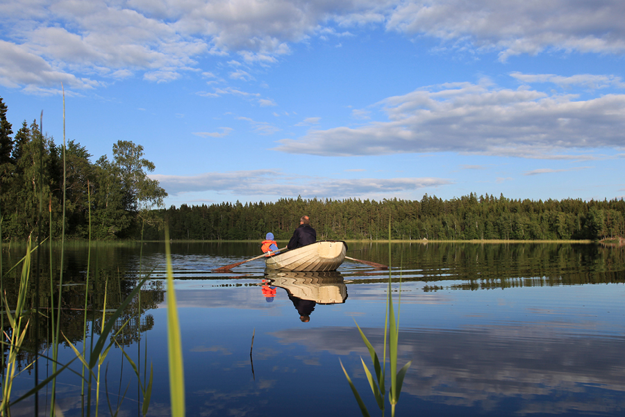 En morfar och barnbarn som åker roddbåt på sjön.
