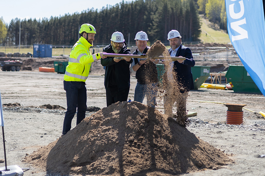 Fyra män håller i en spade och gräver i en grushög.