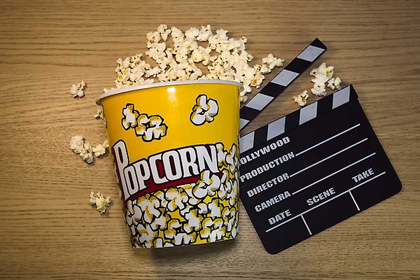 En gul behållare med "Popcorn" på, full av popcorn och en filmklapp med "HOLLYWOOD PRODUCTION" på.