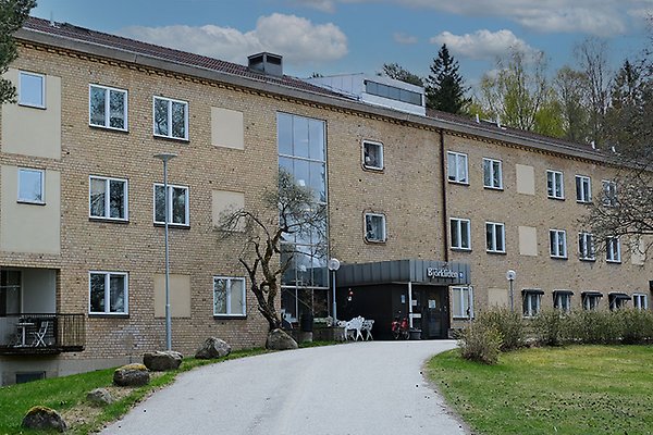 En tegelbyggnad med stora fönster. En grusgång leder fram till ingången.