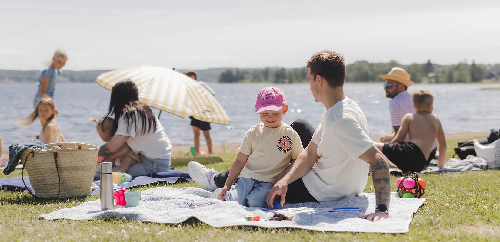 En grupp människor som sitter på filtar på en gräsmatta vid vattnet.