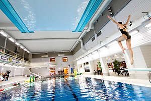 En tjej som hoppar simhopp från en trampolin i ett badhus.
