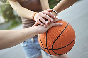 Basketboll och flera händer som håller i den tillsammans.