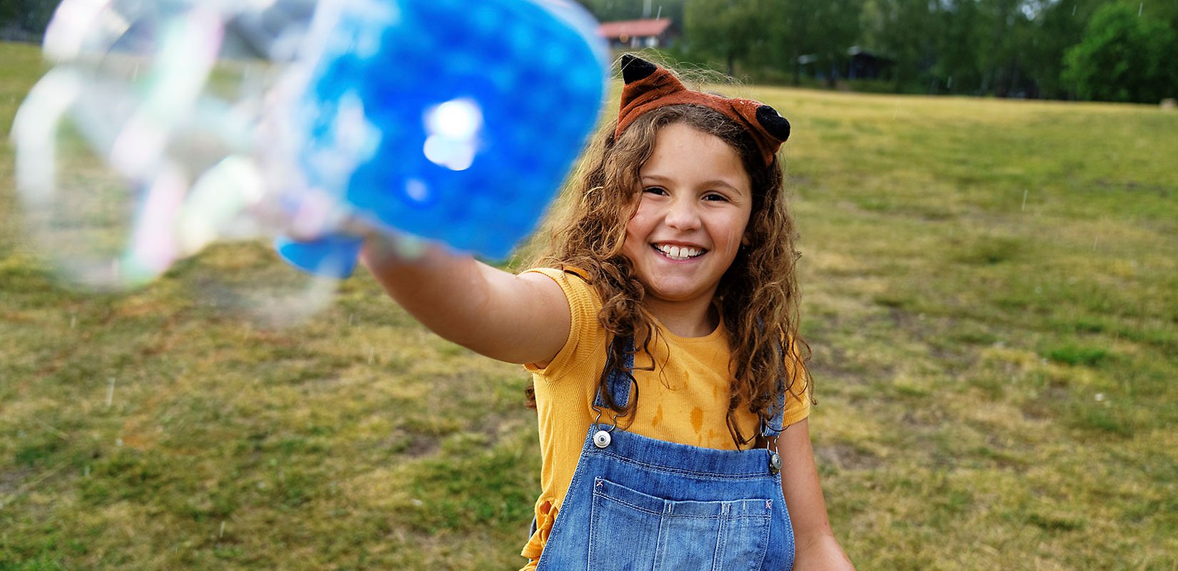 Porträtt av glad flicka som leker med såpbubblor.